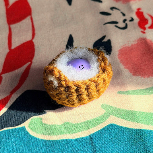 Bonino in a purple swirl color. Nestled in a crochet basket. Side facing.