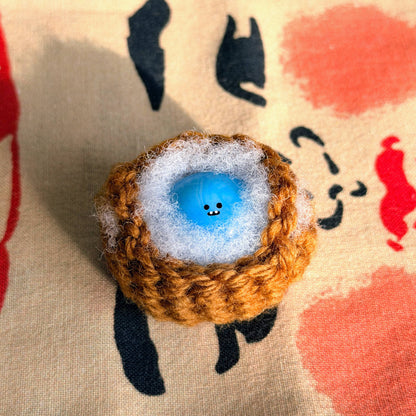 Bonino in a blue swirl color. Nestled in a crochet basket. Front facing.