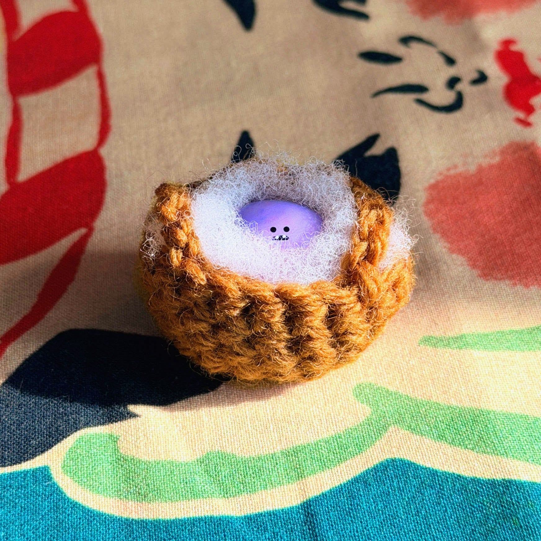 Bonino in a purple swirl color. Nestled in a crochet basket. Front facing.